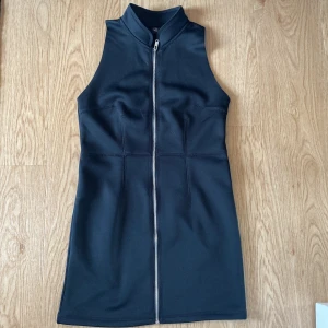 Svart ärmlös kortklänning med dragkedja från Cheap Monday storlek S - Svart, tight och ärmlös kortklänning med hög krage och hel dragkedja framtill. Klänningen har en sportig vibe och markerade sömmar som ger en snygg siluett. Perfekt för dig som gillar minimalistisk och edgy stil.