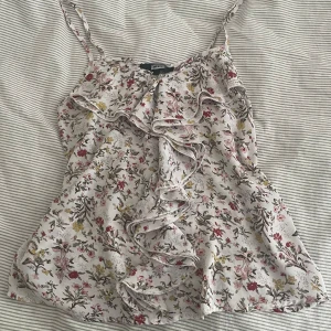 Blommig linnetopp med volang - Supersöt linnetopp från Bik Bok med blommigt mönster i vitt, rosa, rött och gult. Toppen har tunna axelband och en stor volang framtill som ger en romantisk vibe. Perfekt för varma dagar och lätt att matcha med jeans eller kjol.