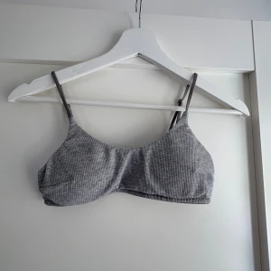 Grå ribbad bralette - Supersnygg grå ribbad bralette med tunna justerbara axelband. Toppen har en enkel och stilren design med diskret mönster och mjukt material som sitter skönt mot kroppen. Strl 36. Endast använd fåtal gånger. 