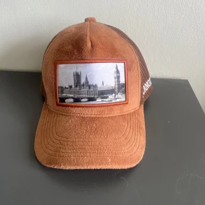 Keps (limiterad) - Snygg brun keps från pianotti! med mesh på sidorna och baksidan. Framsidan har en patch med svartvit bild av London och Big Ben. Justerbar snapback och mjuk, framsidan ger en unik look. Kontakta mig vid minsta fundering😃