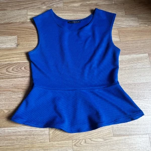 Blå peplumtop  - Snygg blå peplumtop från Atmosphere med ärmlös design och rund halsringning. Toppen har en strukturerad yta och markerad midja som ger en fin siluett. Perfekt att styla med jeans eller kjol för en trendig look.