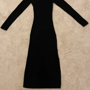 Svart ribbad långklänning - Säljer en svart ribbad långklänning med lång ärm och hög hals. Klänningen har en tight passform och en slits nertill för extra edge. Perfekt för dig som gillar stilrena och minimalistiska plagg med en snygg siluett.
