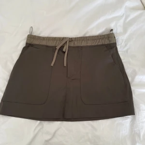 Beige shorts med snörning - Snygga grön  kjol med elastisk midja och snörning framtill. De har två stora fickor framtill och är perfekta för varma dagar. Stilen är enkel och avslappnad, passar dig som gillar en clean look.