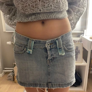 Ljusblå jeanskjol med nitar och patchar - Trendig ljusblå jeanskjol med slitna detaljer, patchar i ljusblått tyg och coola silverfärgade nitar baktill. Kjolen har rå kant nertill, stora bakfickor och unika sömmar i blått. Perfekt för dig som gillar en cool och personlig stil.