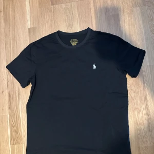 Svart t-shirt Polo Ralph Lauren - Svart t-shirt från Polo Ralph Lauren med klassisk passform och liten broderad logga på bröstet. Slim fit-modell i mjuk bomull, perfekt för en clean och stilren look. Rund halsringning och korta ärmar.