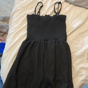 Svart smockad sommarklänning H&M - Svart kortklänning från H&M med smockad överdel och tunna axelband. Klänningen har en luftig kjol och är perfekt för varma dagar. Enkel och stilren design som är lätt att matcha med accessoarer.