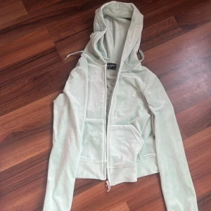 Mintgrön Juicy Couture hoodie XS - Supermjuk mintgrön hoodie från Juicy Couture i velour med dragkedja och huva. Klassisk JC-logga på bröstet och snygg J-detalj på dragkedjan. Perfekt croppad passform och långa ärmar. En riktig Y2K-vibe för dig som älskar comfy men trendigt.