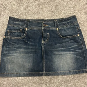 Mörk jeanskjol från Yishion - Snygg mörkblå jeanskjol från Yishion i klassisk femficksmodell. Kjolen är i 100% bomull med slitna detaljer och kontrastsömmar. Säljer då den aldrig kommit till användning 