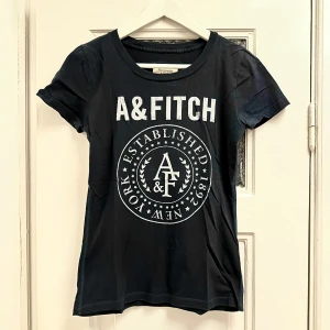 Mörkblå t-shirt från Abercrombie & Fitch  - Mörkblå T-shirt från Abercrombie & Fitch med vitt tryck. Storlek M men passar främst S.