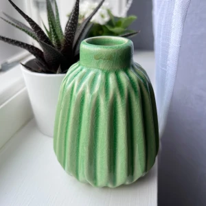 Liten grön vas - Liten grön keramikvas med räfflad, organisk form och glansig yta. Vasen har ett retroinspirerat utseende och passar perfekt som inredningsdetalj för dig som gillar unika och färgglada prylar. Perfekt för små blommor eller som dekoration i ditt rum. Önskar du veta exakta mått? Tveka inte at höra av dig!
