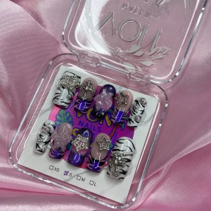 Z3br@Babe (S);Medium Square - Set i storlek S: 15 mm, 11,5 mm, 12 mm, 11 mm, 9 mm. Naglarna har lila, rosa och svartvitt zebramönster, dekorerade med 3D-stjärnor, kors och pärlor i silver. Mix av glansiga och matta ytor, vissa med glittereffekt. 