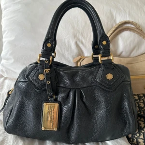 Svart Q Classic Baby Groove väska! - Så snygg svart klassisk handväska i nyskick från Marc by Marc Jacobs i äkta läder med gulddetaljer och dubbla handtag. Väldigt snygg färg som passar till allt, den perfekta sommarväskan som rymmer mycket men är smidig och nätt. Lilla modellen Q Classic. Inga repor eller hål på väskans läder. Otroligt välbevarad vintage modell! Perfekt för att ge en stilren touch till din outfit. Skriv privat för fler bilder. Mått 34x18x12 (undersida). Kan hämtas hemma hos mig i Nacka eller skickas 🤍