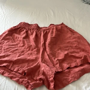 Rosa loose shorts från BikBok - Superbekväma rosa shorts från BikBok i loose fit med elastisk midja och lätt rynkad kant upptill. Perfekta för varma dagar och chill vibes. Tillverkade i ett mjukt och svalt material som känns skönt mot huden.