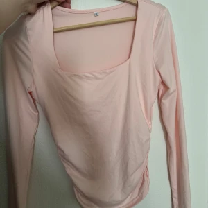 Ljusrosa långärmad topp med fyrkantig ringning - Säljer en ljusrosa långärmad topp med snygg fyrkantig ringning. Toppen är figurnära och har en enkel, stilren design som passar perfekt till jeans eller kjol. Mjuk och skön i materialet, perfekt för vår och sommar.