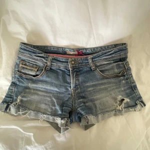 Blå jeansshorts från Stradivarius - Snygga blå jeansshorts från Stradivarius med slitna detaljer och fransig kant. Klassisk femficksmodell med låg midja och knappstängning. Perfekta för sommardagar och har en cool, avslappnad vibe. ❤️❤️