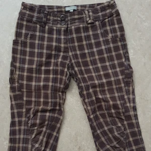Byxor - Bruna byxor med rutigt mönster i beige och blått från Kids by Lindex. Byxorna har normal passform, raka ben och två knappar i midjan. Perfekta för dig som gillar en avslappnad men ändå stilren look.