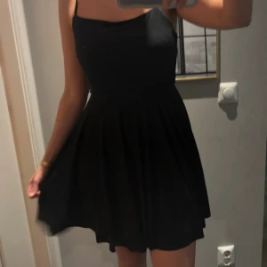 Somrig svart klänning med tunna axelband - Supersnygg svart kort klänning med tunna axelband och korsade band i ryggen. Klänningen har en figurnära överdel och utställd kjol som ger en riktigt fin siluett. Älskar denna men används knappt tyvärr. Skulle passa även en storlek M