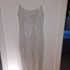Glittrig silverklänning - Supersnygg långklänning från Bella Barnett i silver med tunna axelband. Klänningen är täckt av glittrande paljetter och har en figurnära passform. Perfekt för dig som vill sticka ut med en elegant och festlig look. Använd 1 gång.