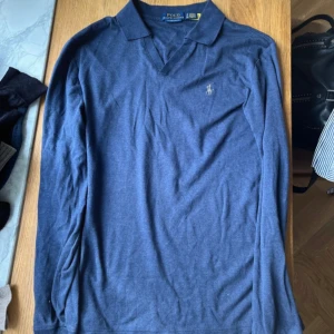 Blå pikétröja från Polo Ralph Lauren - Snygg blå långärmad pikétröja från Polo Ralph Lauren i slim fit. Tröjan är tillverkad i 100% bomull och har klassisk krage samt broderad logga på bröstet. Perfekt för dig som gillar stilren och tidlös design.