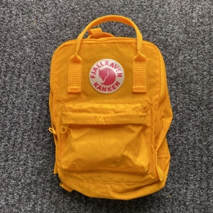 Gul Kånken Mini ryggsäck från Fjällräven - Säljer en ikonisk Kånken Mini ryggsäck från Fjällräven i en riktigt poppig gul färg. Väskan har klassisk fyrkantig form, stort huvudfack, dragkedja och en mindre ficka framtill. Broderad logga och justerbara axelremmar. Perfekt storlek för det viktigaste.