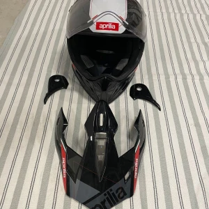 Aprilia svart och vit hjälm - Snygg integralhjälm från Aprilia i svart och vitt med röd logga framtill. Hjälmen har visir och flera utbytbara delar, perfekt för dig som vill sticka ut på vägarna. Helt ny ingår låda osv 