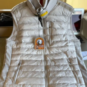 Vit dunväst från Parajumpers - FINNS I ALLA STORLEKAR! Snygg vit dunväst från Parajumpers med quiltad design och hög krage. Västen har dragkedja framtill, två sidofickor med dragkedja och en bröstficka. Perfekt för lager-på-lager och har coola detaljer som gul rem vid halsen.