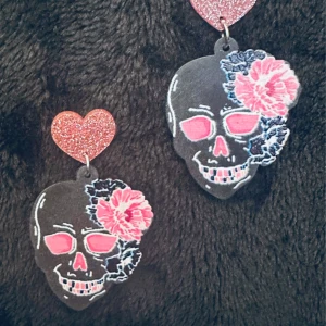 Svarta dödskalleörhängen med rosa glitterhjärtan Akryl Nya  - Nya örhängen i svart akryl med dödskallemotiv, rosa blommor och glittriga hjärtan. En perfekt mix av romantik och alternativ edge. De är lätta att bära trots sin storlek (ca 5 cm långa, 3 cm breda) och sitter bekvämt med stift. Priset är fast – ingen prutning – men jag erbjuder gärna rabatt vid köp av flera saker. Jag rensar smyckesskrinet, så kika gärna på mina andra annonser också!  