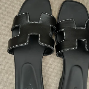 Svarta Oran sandaler - Svarta Oran sandaler med vita sömmar, storlek 38. Nyskick, aldrig använda utomhus.