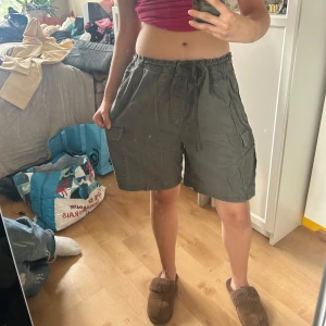 Grå cargoshorts med snörning - Säljer ett par fett snygga grågröna cargoshorts från märket bruebeck. Shortsen har flera stora fickor på sidorna och baktill. Shortsen passar väldigt fint till både tighta och baggy överdelar! Väldigt sköna att använda nu i sommarvärmen🌼Storleken är XL, men om man knyter de bra så kan någon med S och uppåt också använda de!