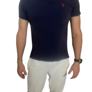 Marinblå piké - Snygg marinblå pikétröja från Polo Ralph Lauren i storlek XL i barnstorlek så passar typ S. Klassisk design med korta ärmar, krage och knappar framtill. Tröjan har den ikoniska röda broderade loggan på bröstet och är tillverkad i mjuk bomull. Perfekt för en clean och sportig look.