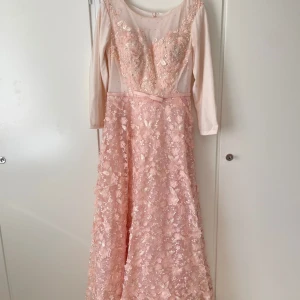 Ljusrosa festlig klänning med spets och pärlor - Drömmig ljusrosa långklänning med blommig spets, pärlor och paljetter på överdelen. Klänningen har långa ärmar, markerad midja med liten rosett och transparent mesh upptill. Perfekt för bal eller student. Kjolen är utsvängd och täckt av 3D-blommor. Strl L. Använt 1 gång och är fortfarande i väldigt fint skick. Inbyggd Bh, ej genomskinlig.  Köpt för 4000kr utomlands, säljer för halva priset.