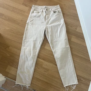 Beige jeans från ONLY med råa benslut - Snygga beige jeans från ONLY med hög midja och raka ben. Jeansen har klassisk femficksdesign och coola råa benslut för en trendig look. Passar perfekt till sneakers eller boots.