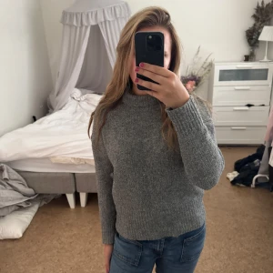 Grå stickad tröja med semi-hög krage - Mysig grå stickad tröja med lite högre krage och långa ärmar. Tröjan har en enkel och clean look med ribbade muddar vid ärmslut och nederkant. Perfekt till kallare kvällar eller vintrar. Nopprig men fixar vid intresse.