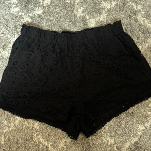 Svarta spetsiga shorts från H&M - Svarta shorts från H&M i storlek 36 med snygg spets och broderade detaljer. De har elastisk midja och en loose passform, perfekta för varma sommardagar. 