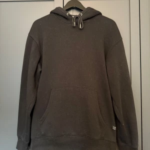 Svart hoodie från Jack & Jones - Svart hoodie från Jack & Jones med klassisk känguruficka och snörning i huvan. 