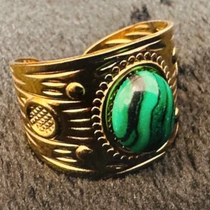 Ny Boho gyllene ring med grön sten – justerbar och iögonfallande -  Statementring i guldfärgad metall med vackert infattad grön sten (troligtvis malakit). Den bohoinspirerade designen med etsade detaljer ger ringen en elegant vintagekänsla. Justerbar storlek och bekväm att bära. Höjd ca 1,8 cm. Priset är fast – ingen prutning – men jag erbjuder rabatt vid köp av flera saker. Jag rensar smyckesskrinet, så passa på att kolla mina andra annonser också!  ⸻ 