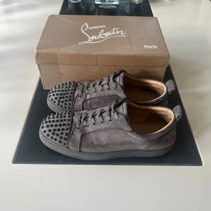 Christian Louboutin Skor - Christian Louboutin sneakers i mörkgrå mocka med ikoniska nitar på tårna. Skorna är stilrena men har små tecken på användning. Storlek 44, extra nitar ingår samt original kartong medföljer! 