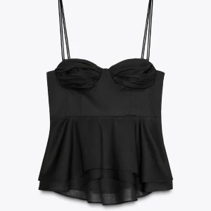 Svart volang topp med tunna axelband - Supersnygg svart topp från Zara med tunna dubbla axelband och volang nertill. Kuporna är lätt rynkade för en cool look och toppen har en figurnära passform upptill. Perfekt att styla med jeans eller kjol för en trendig vibe. Den är aldrig använd och säljs pågrund av fel storlek. Toppen är mindre i storleken än vanligt.