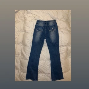 Blå bootcut jeans med nitar - Snygga blå bootcut jeans, från shein, med coola detaljer på bakfickorna, som nitar och knappar. Jeansen har en klassisk femficksmodell och lätt slitning framtill och baktill. Dem är storlek S. Jeansen är även aldrig använda. Perfekta för dig som vill ha en trendig och bekväm look. 