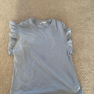 Ljusblå volangtopp från Pull&Bear XS - Supersöt ljusblå topp från Pull&Bear i storlek XS. Toppen har volangdetaljer på ärmarna som ger en extra touch och är tillverkad i mjuk bomull. Perfekt för dig som gillar en enkel men ändå trendig stil. Härlig färg!