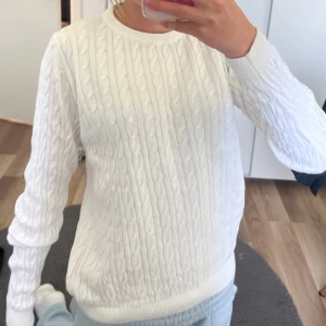 Vit kabelstickad tröja från Ullared - Vit kabelstickad tröja från Ullared med klassiskt mönster och rund halsringning. Tröjan har långa ärmar och ribbade muddar vid ärmslut och nederkant. Perfekt för lager-på-lager och en clean look.