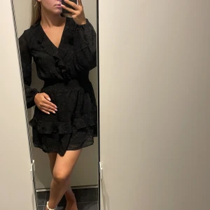 Svart volangklänning med v-ringning - Supersnygg svart kortklänning med v-ringning och volangdetaljer från Nelly, helt oanvänd med lapparna kvar.🖤