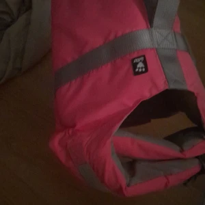 Hundflytväst från Hurtta - Säljer en rosa hundflytväst från Hurtta med grå detaljer och justerbara band. Flytvästen är tillverkad i slitstark polyester och har en sportig look med praktiska spännen och reflexdetaljer.