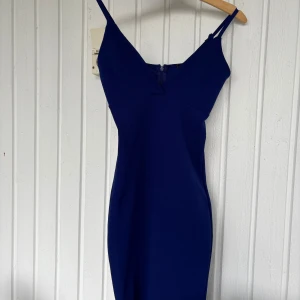 Marinblå klänning från Bik Bok XS - Snygg marinblå klänning från Bik Bok i figurnära modell med smala axelband och v-ringad urringning. Klänningen har dragkedja i ryggen och är tillverkad i ett slätt, stretchigt material. Perfekt för dig som gillar stilrena och enkla plagg.