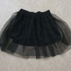 Tyllkjol - Supersöt svart tyllkjol med små guldprickar från mywear baby. Kjolen har resår i midjan och flera lager tyll som ger en fluffig känsla. Perfekt för dig som vill sticka ut lite extra med glittriga detaljer.