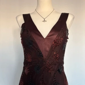 Vintage balklänning - Vintage brun balklänning från Avant garde med v-ringning och breda axelband. Klänningen har glittriga paljettbroderier, samt en figurnära passform. Materialet är tunt och elegant, perfekt för fest eller bal.