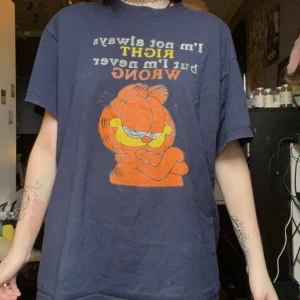 Mörkblå Garfield t-shirt med tryck - Säljer en mörkblå t-shirt med stort Garfield-tryck och texten 'I'm not always right but I'm never wrong' på framsidan. T-shirten har normal passform och korta ärmar. Perfekt för dig som gillar retro och tecknade serier.