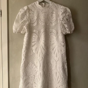 Vit spetsklänning med puffärm - Superfin vit kortklänning med puffärmar och vackert broderat spetsmönster. Klänningen har rund halsringning och är fodrad under, vilket ger en exklusiv känsla. Perfekt för sommarens alla tillfällen!