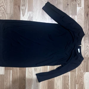 Svart klänning med dragkedja - Säljer en svart, figurnära klänning med trekvartsärm och guldfärgad dragkedja i ryggen. Klänningen har en klassisk och stilren design, perfekt för dig som gillar enkel elegans. Materialet känns mjukt och följsamt.  Säljes i bra skick! Totallängd 82 cm  Kommer från djurfritt hem!