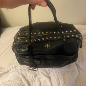 Svart handväska med nitar från Zadig & Voltaire - Cool svart handväska i skinn från Zadig & Voltaire med silverfärgade nitar och dragkedja upptill. Väskan har dubbla handtag och nitar. Rymlig och stor 